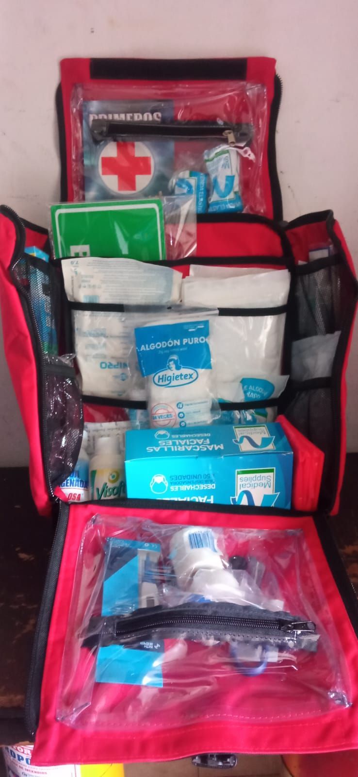 Botiquín rojo abierto con suministros médicos variados y una cruz blanca en la parte superior.