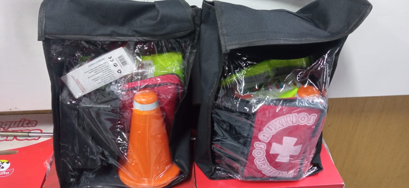 Dos bolsas negras con artículos variados, una con un cono naranja y la otra con un emblema rojo de estilo suizo.
