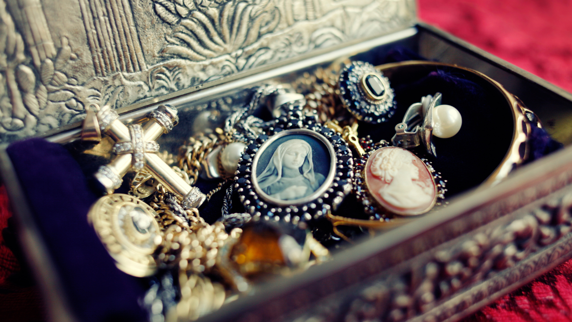 A box filled with lots of jewelry is sitting on a red cloth.