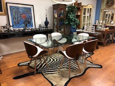 A dining room with a glass table and chairs and a zebra print rug.