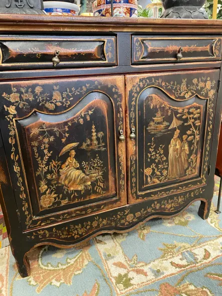 A black and gold cabinet with drawers and doors is sitting on a rug.