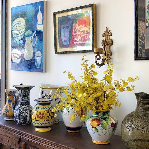 A table with a bunch of vases and paintings on the wall.