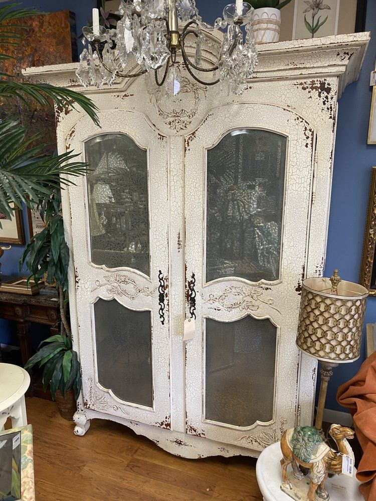 A white cabinet with glass doors is sitting in a living room next to a lamp.