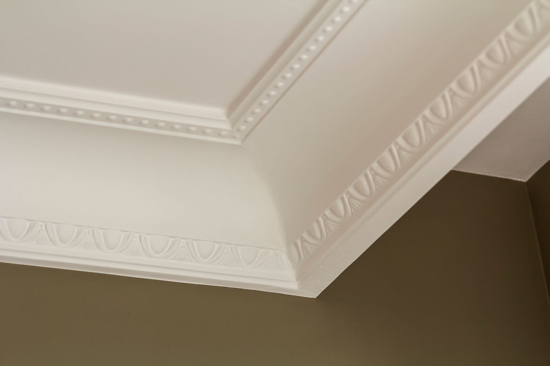 Close-up detail of ornamental white crown molding painted on the ceiling of a white room, adding a decorative touch.