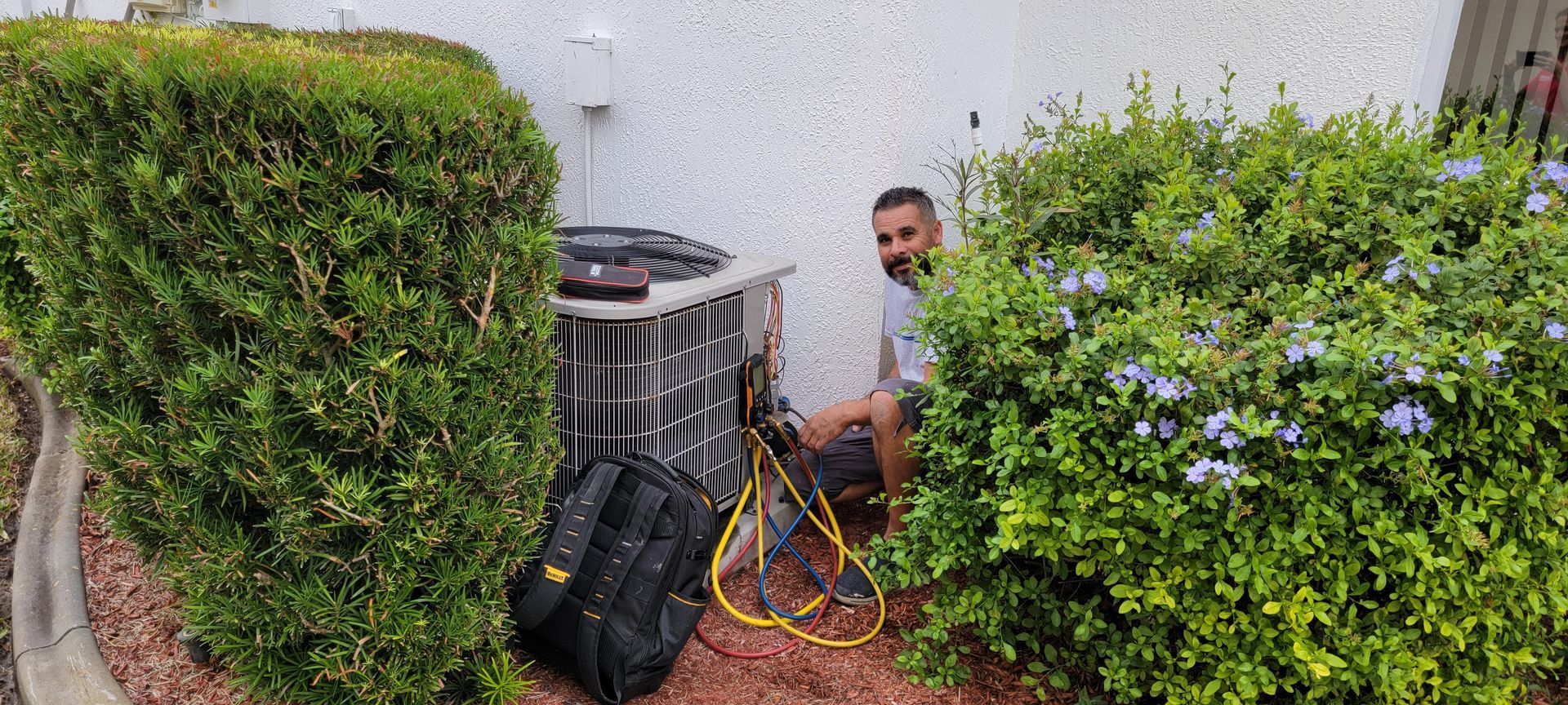 A man is working on an air conditioner in a bush.