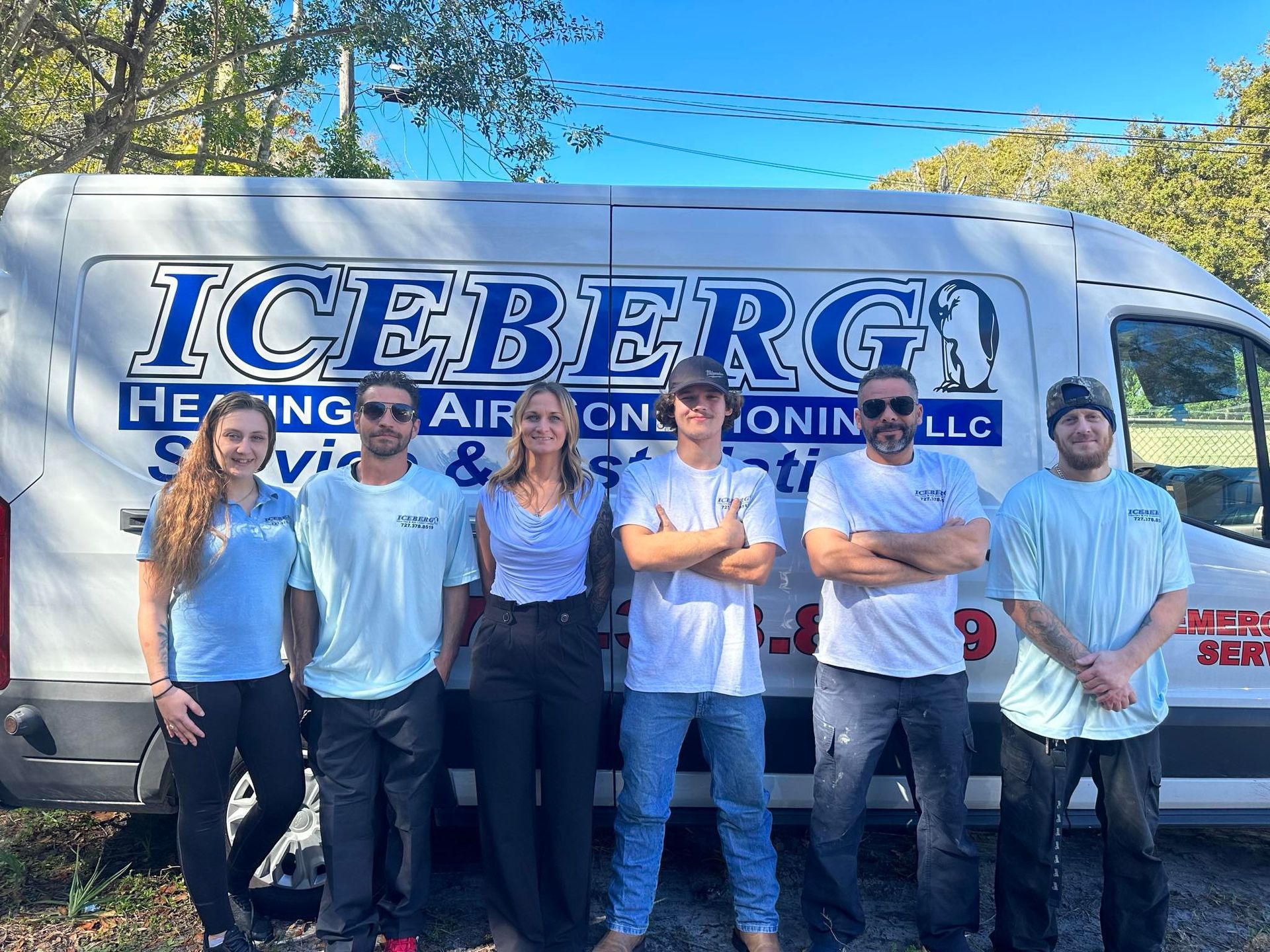A group of people standing in front of an iceberg heating and air conditioning van.