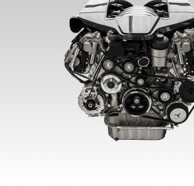 Close-up of a shiny chrome car engine with belts and pulleys, against a gray background | Libertyville Kar Care