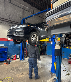 Mechanic working on a black car lifted in a garage; blue lift, gray walls, and equipment | Libertyville Kar Care