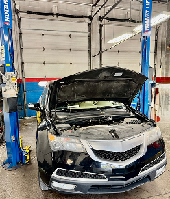 Black car with open hood in a mechanic shop, raised on a lift | Libertyville Kar Care