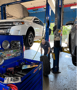 Mechanic changing a tire in a car repair shop; white SUV on lift, blue toolbox in foreground | Libertyville Kar Care