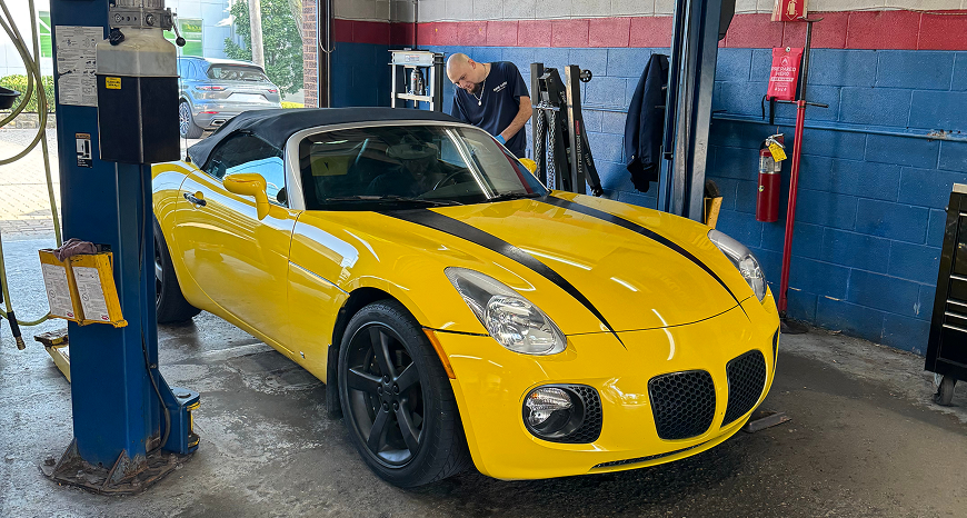 Yellow convertible car in a garage, being worked on by a person in a blue shirt | Libertyville Kar Care