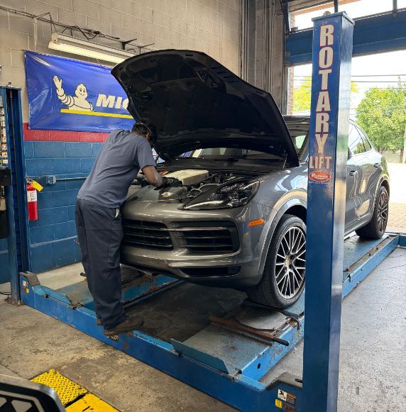 Mechanic working on a gray Porsche Cayenne SUV inside a garage, raised on a blue lift  | Libertyville Kar Care