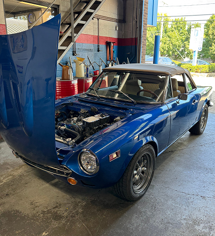 Blue convertible Fiat Spider with hood open in a garage, showcasing the engine | Libertyville Kar Care