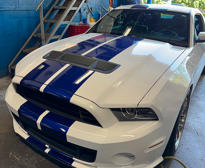 White Ford Mustang with blue racing stripes, parked in a garage | Libertyville Kar Care