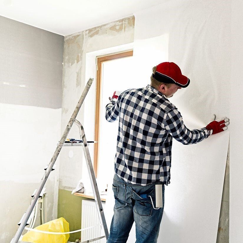 A man in a plaid shirt is working on a wall.