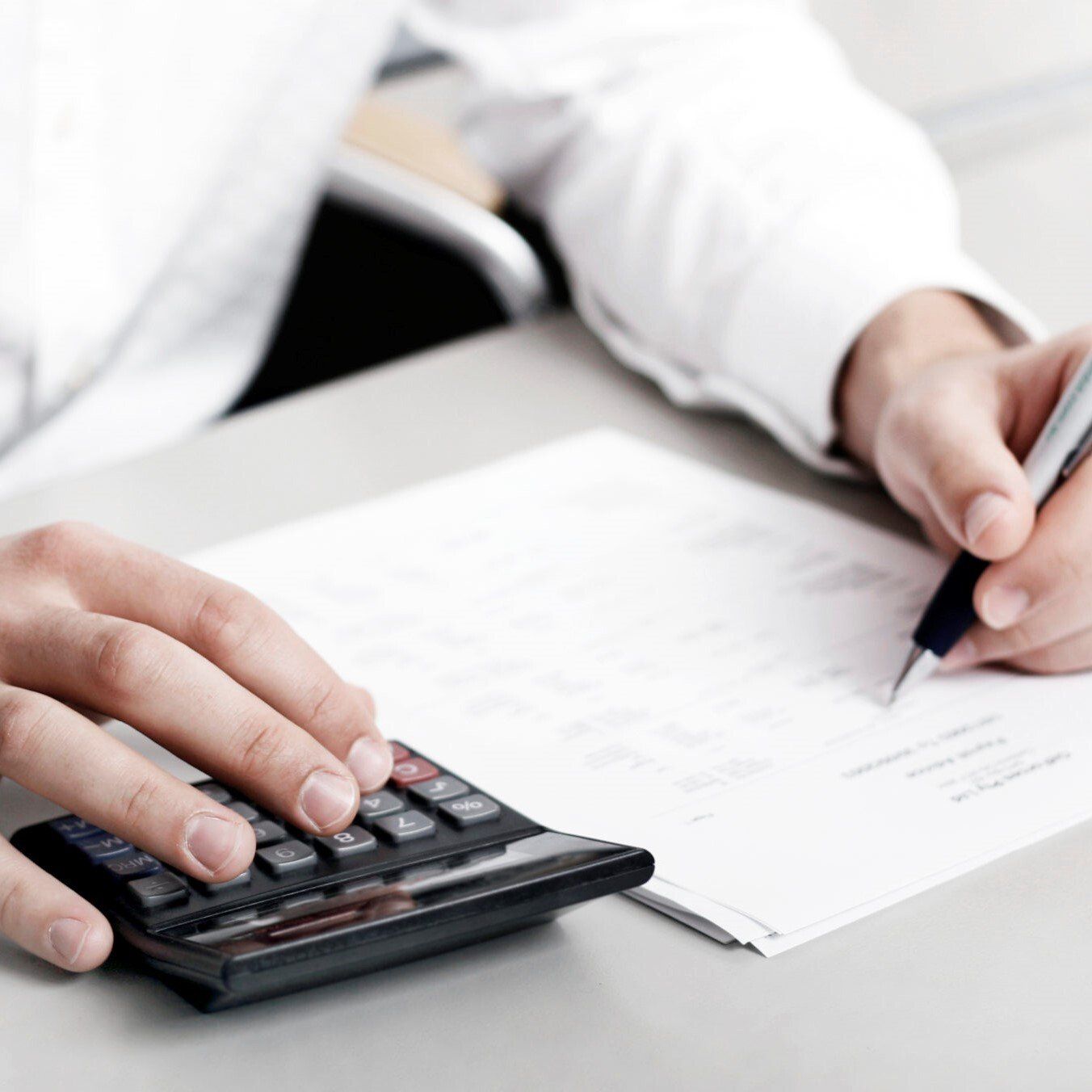 A person is using a calculator and writing on a piece of paper