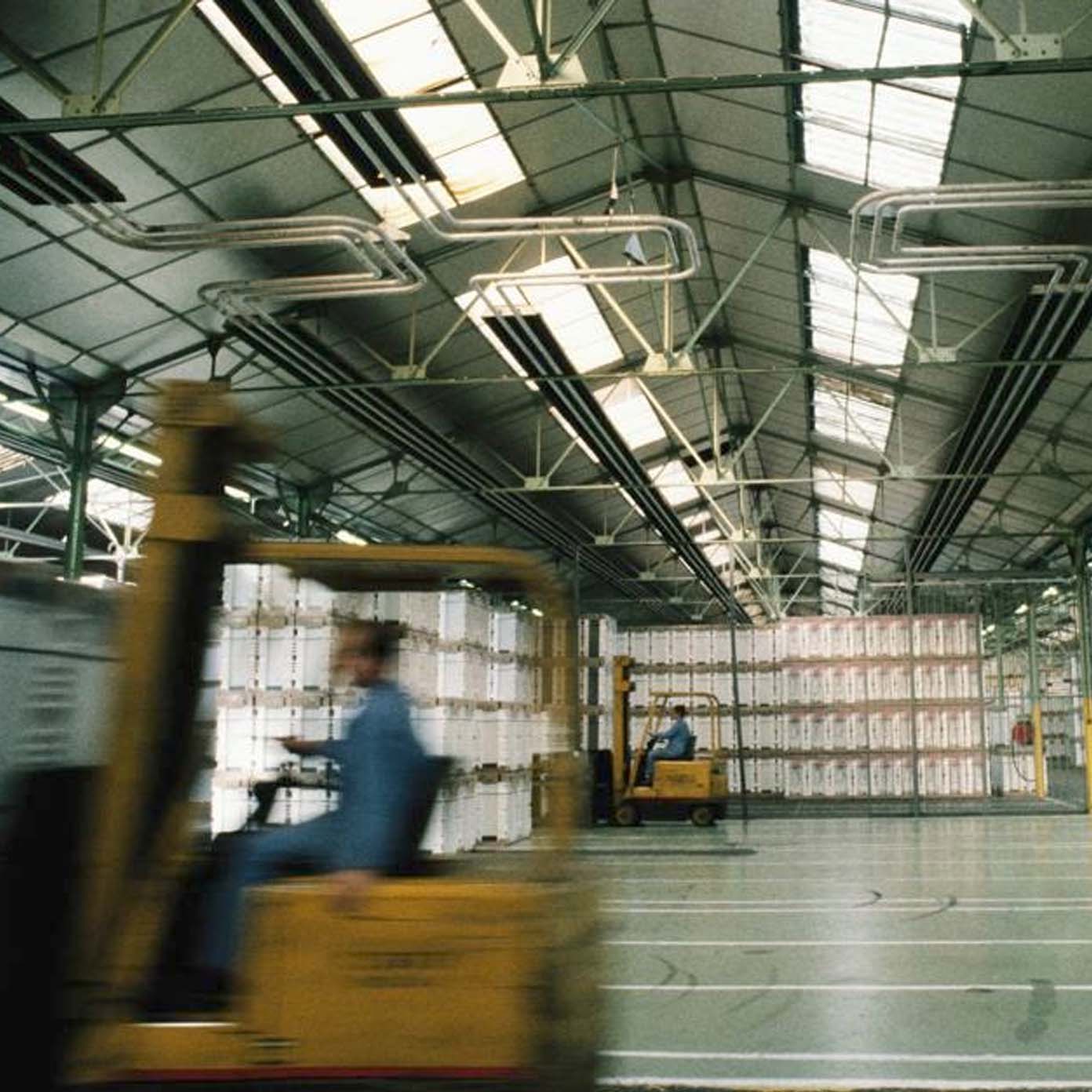 A man driving a yellow forklift in a large warehouse