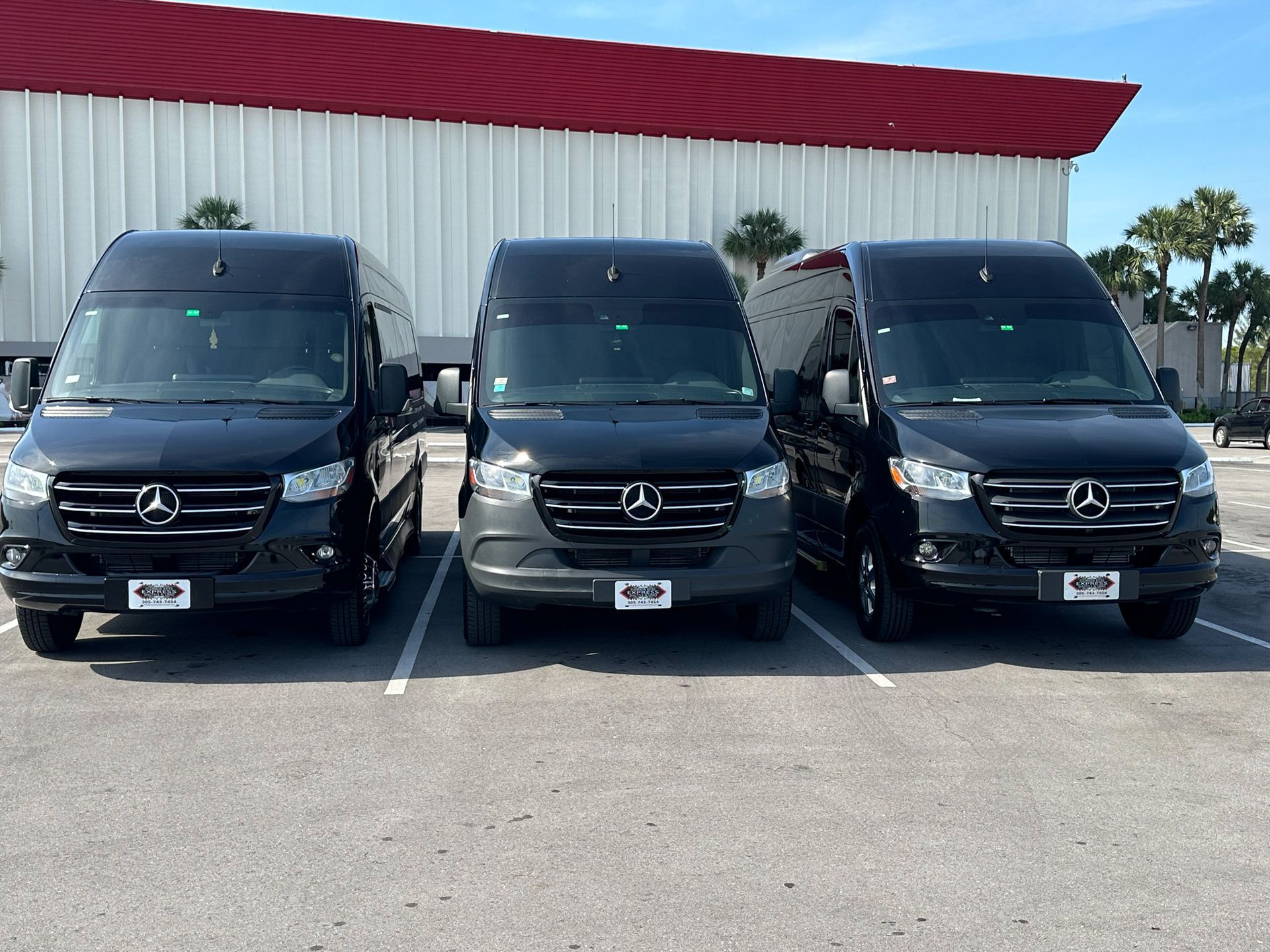 Three black Mercedes-Benz vans parked in a lot in front of a red-roofed building.
