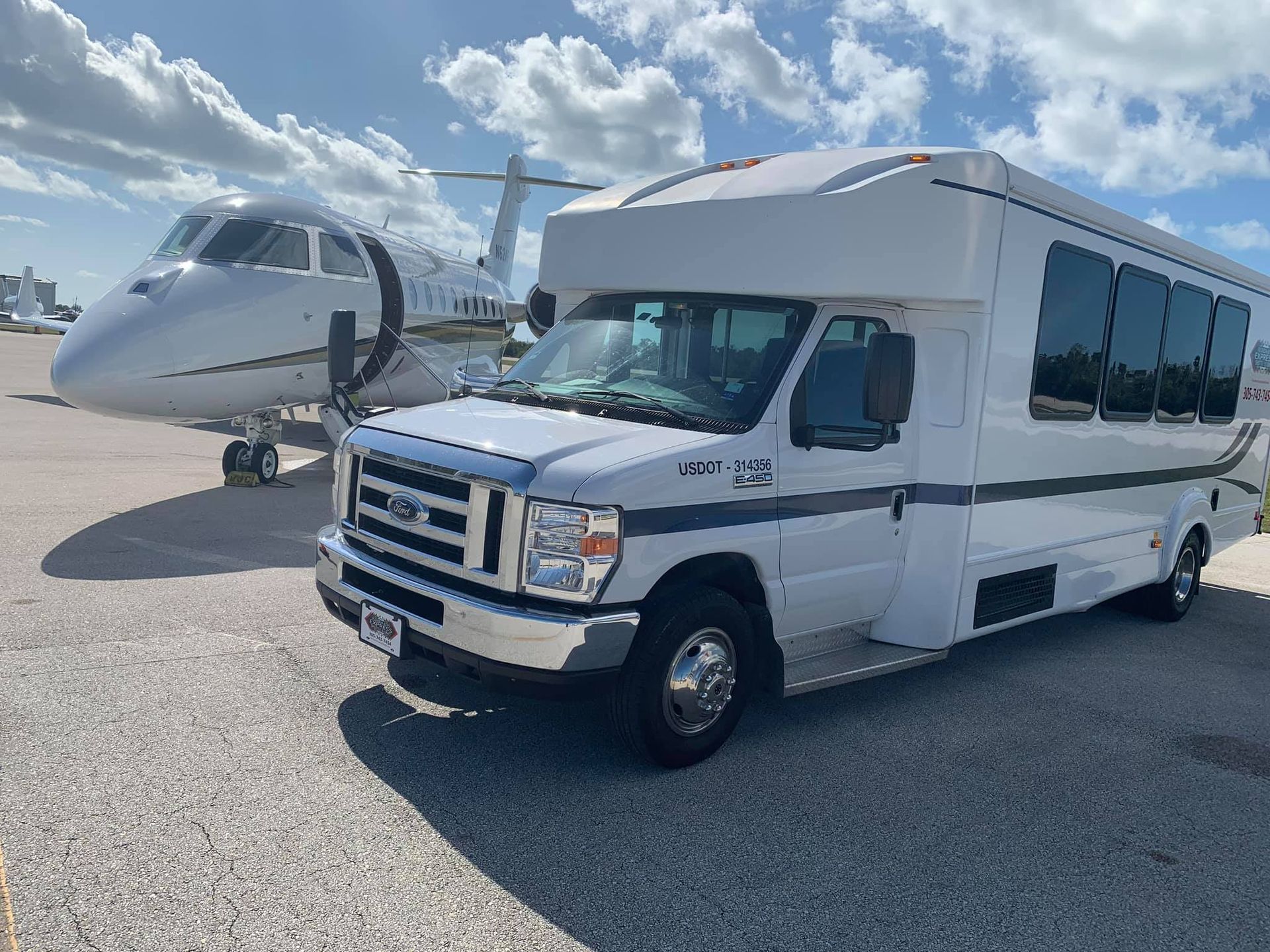 White shuttle bus parked next to a private jet on a sunny tarmac.