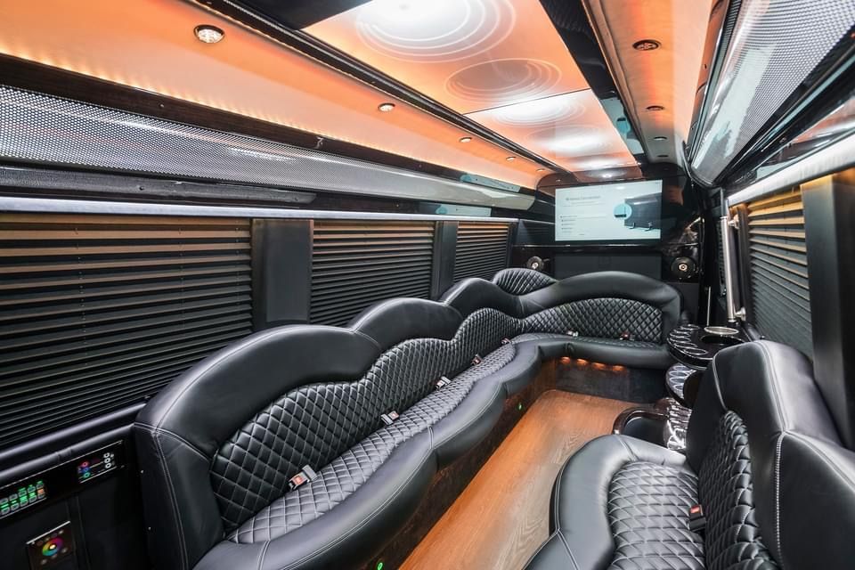 Inside of a luxurious black limousine with diamond-stitched leather seating and a TV screen.