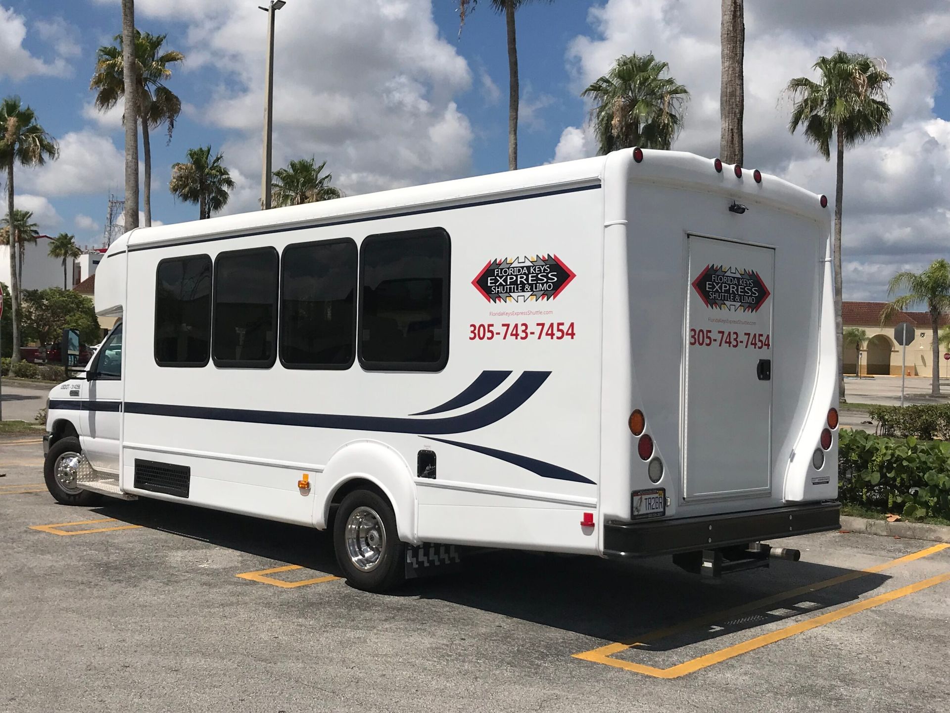 White shuttle bus with dark windows and phone number on the side, parked outside.