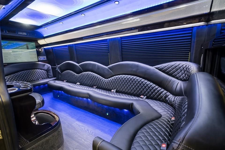 Luxurious black interior of a van with diamond-stitched seating, blue lights, and window shades.
