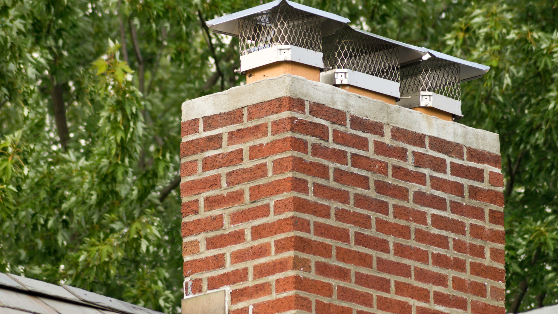 A brick chimney on top of a roof with trees in the background.
