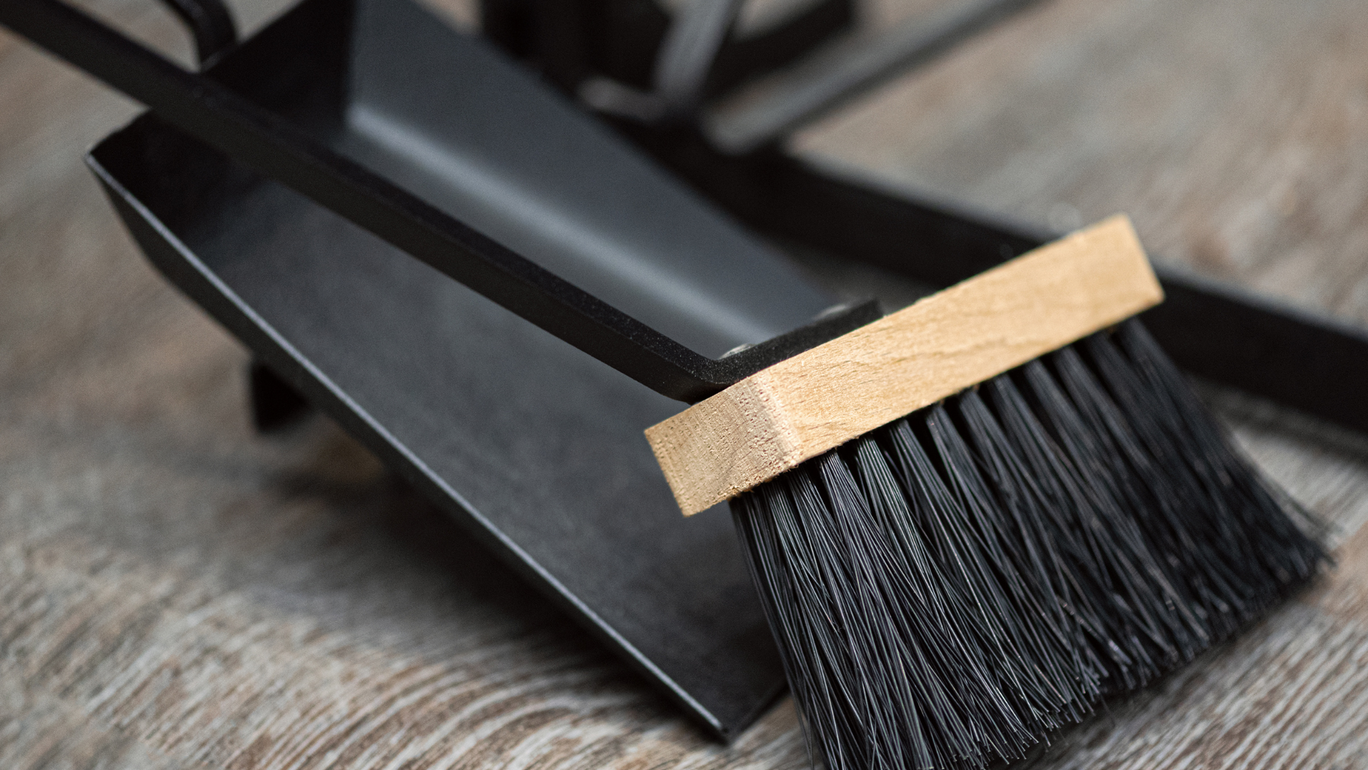 A black brush with a wooden handle is sitting on a wooden table.