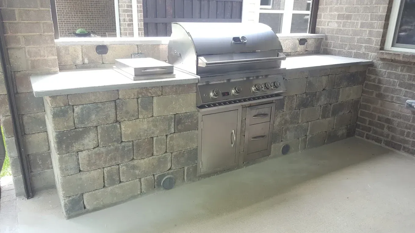An outdoor kitchen with a grill and a brick wall.