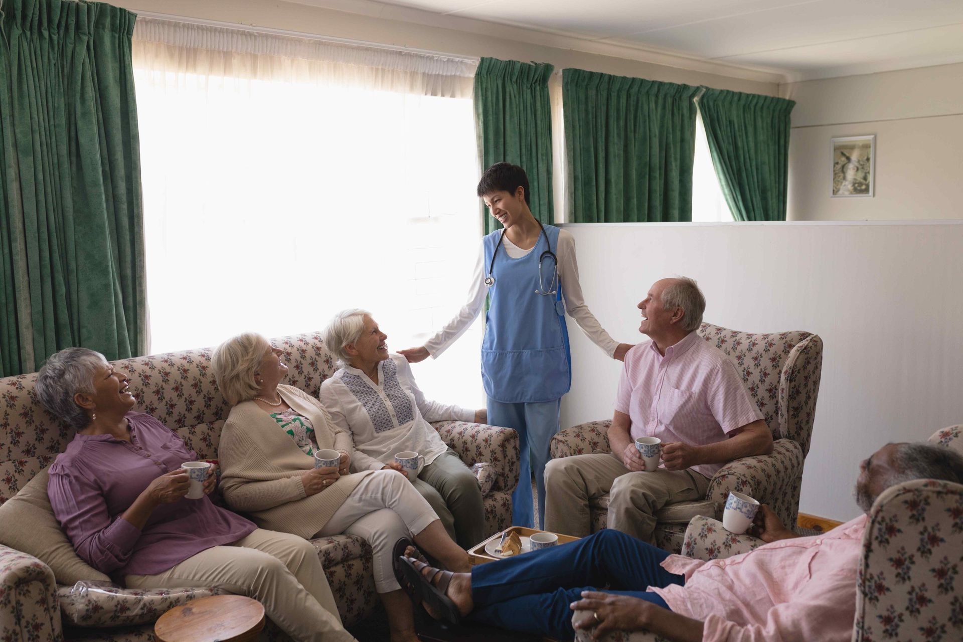 A group of elderly people are sitting on couches in a living room with a nurse.