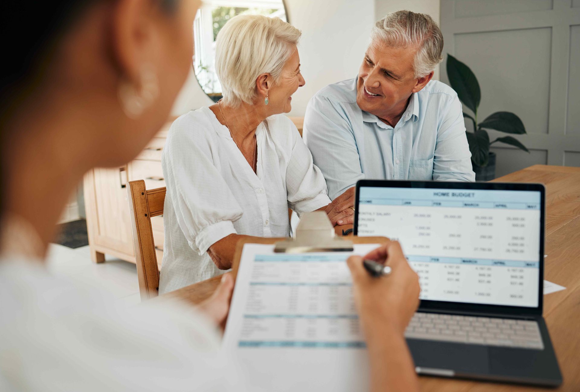 An elderly couple is sitting at a table looking at a laptop computer with a financial specialist.