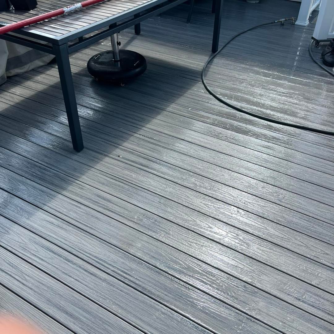 Wet gray composite decking with a metal table, umbrella stand, and hose.