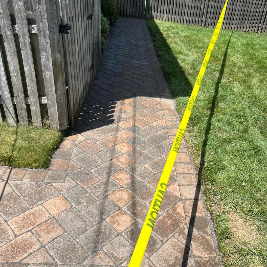 Brick walkway next to a wooden fence and lawn. Yellow tape blocks access to the right.
