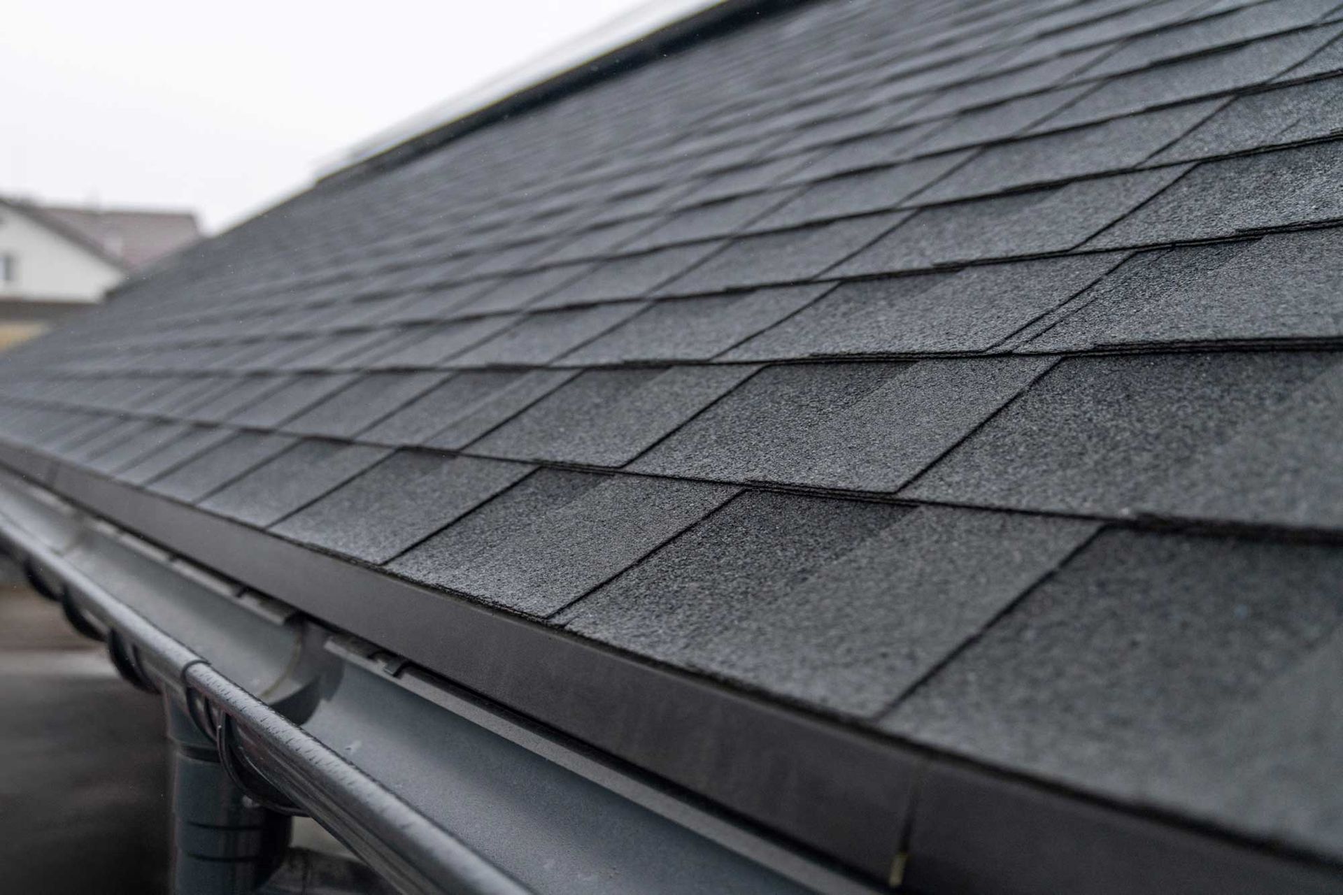 Close-up of a dark asphalt shingle roof with a gutter along the edge. Close-up of a dark asphalt shingle roof with a gutter along the edge.