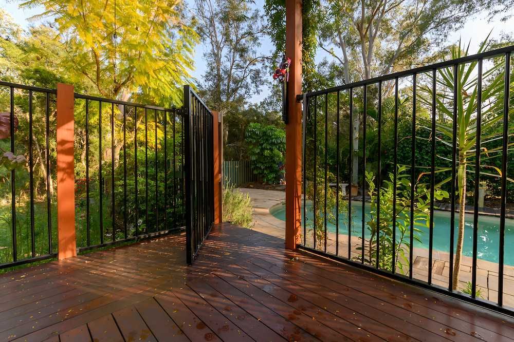 A Wooden Deck With a Metal Fence and a Pool in the Background — Slim Fox Home Improvements in Mooroobool, QLD