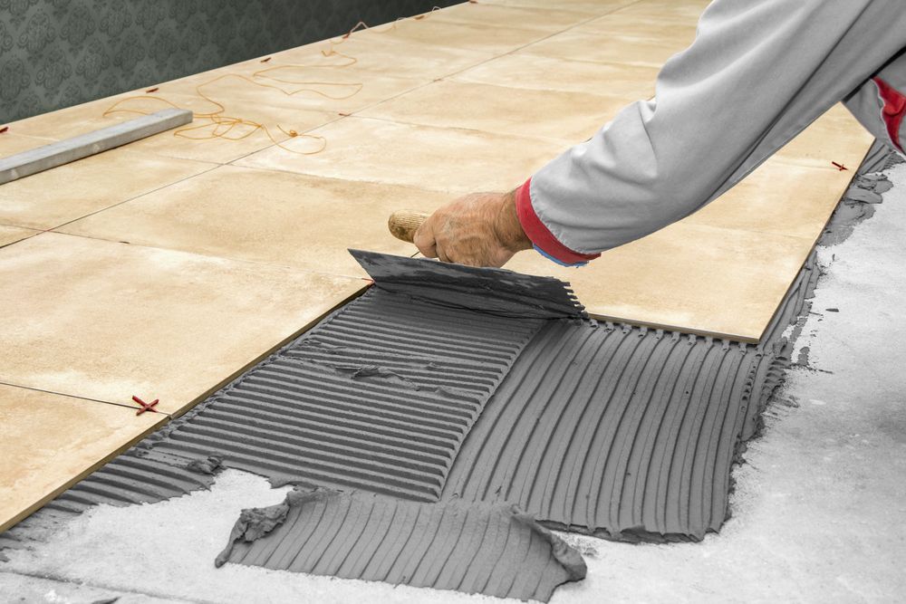 A Person is Laying Tiles on a Floor With a Trowel — Slim Fox Home Improvements in Mooroobool, QLD