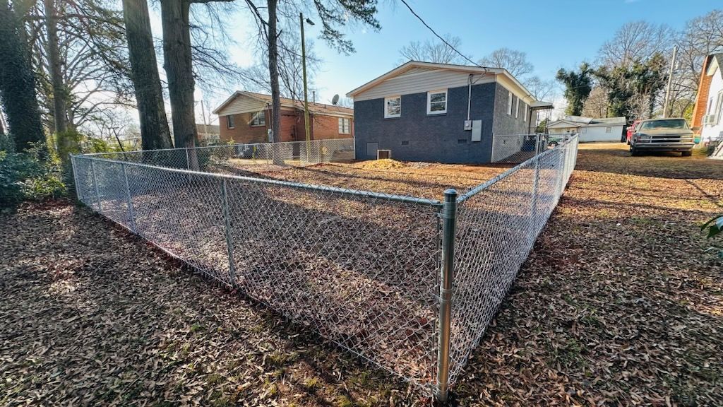 A chain-link fence surrounds a house with a blue-gray exterior, a yard with leaves.