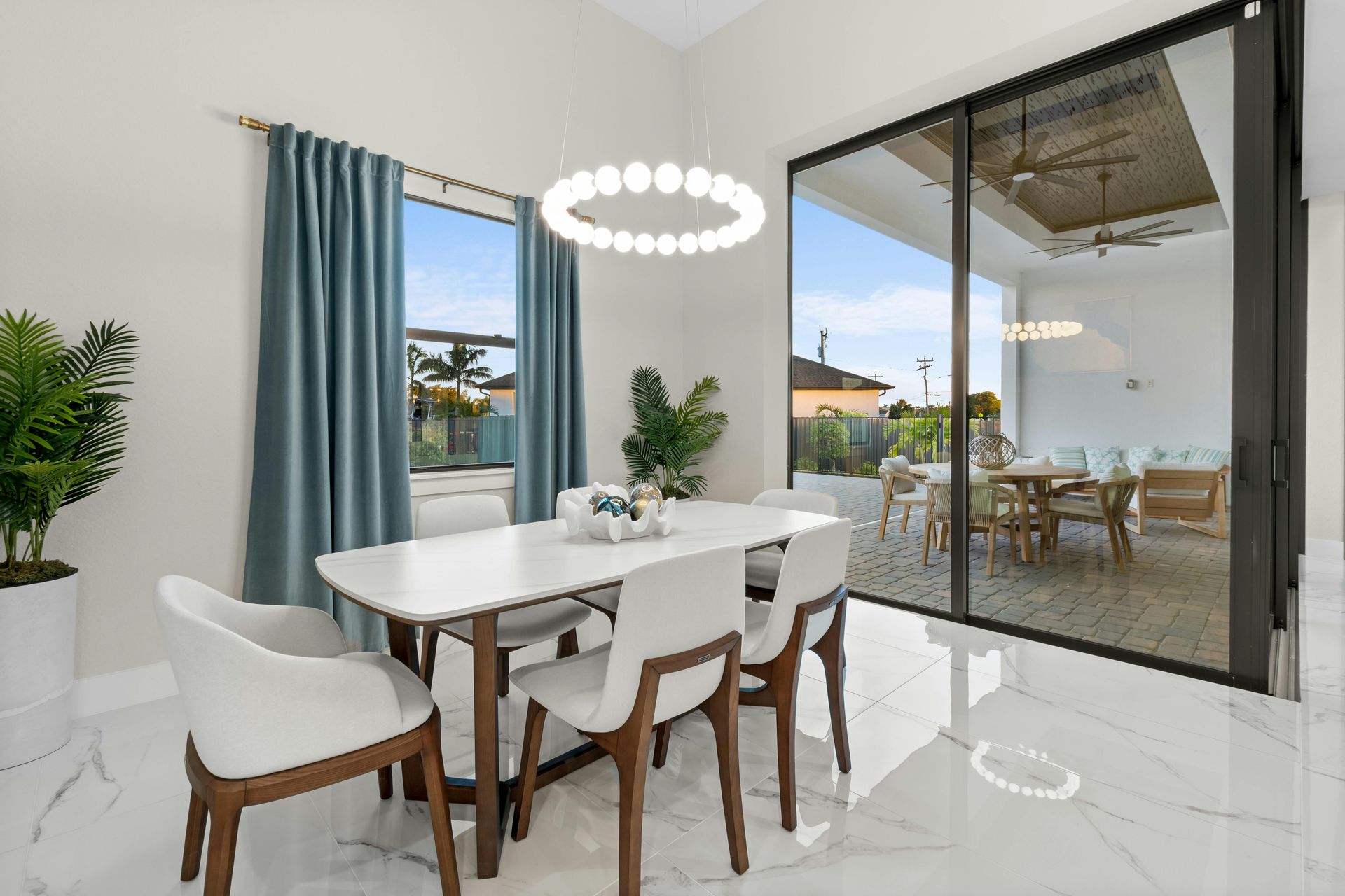 Dining room with white table, chairs, blue curtains, and sliding glass door to an outdoor patio.
