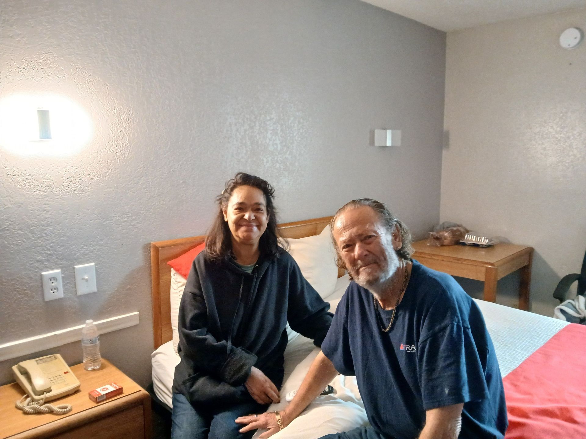 A man and a woman are sitting on a bed in a hotel room.