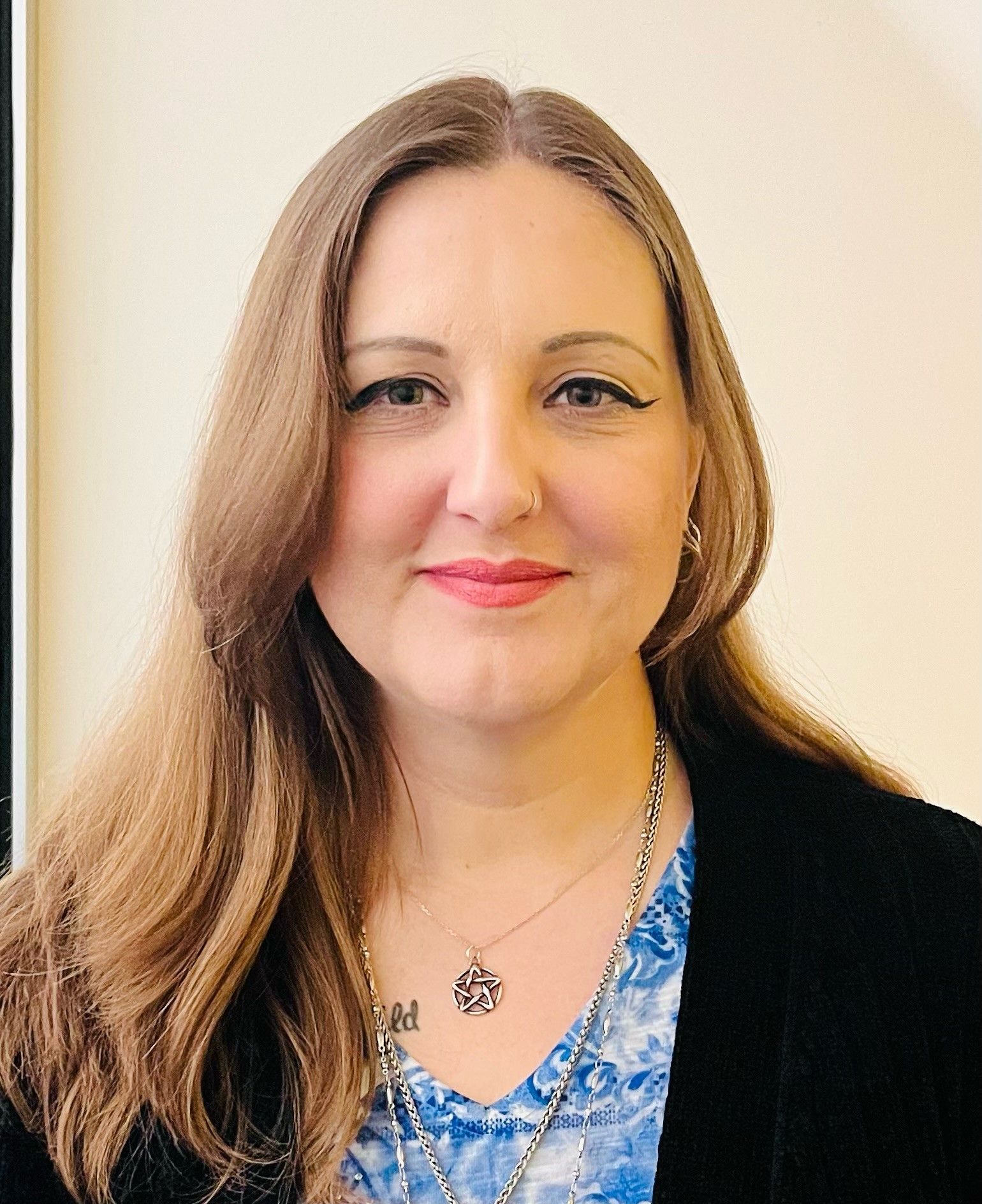 A woman wearing a blue shirt and a black jacket is smiling for the camera.