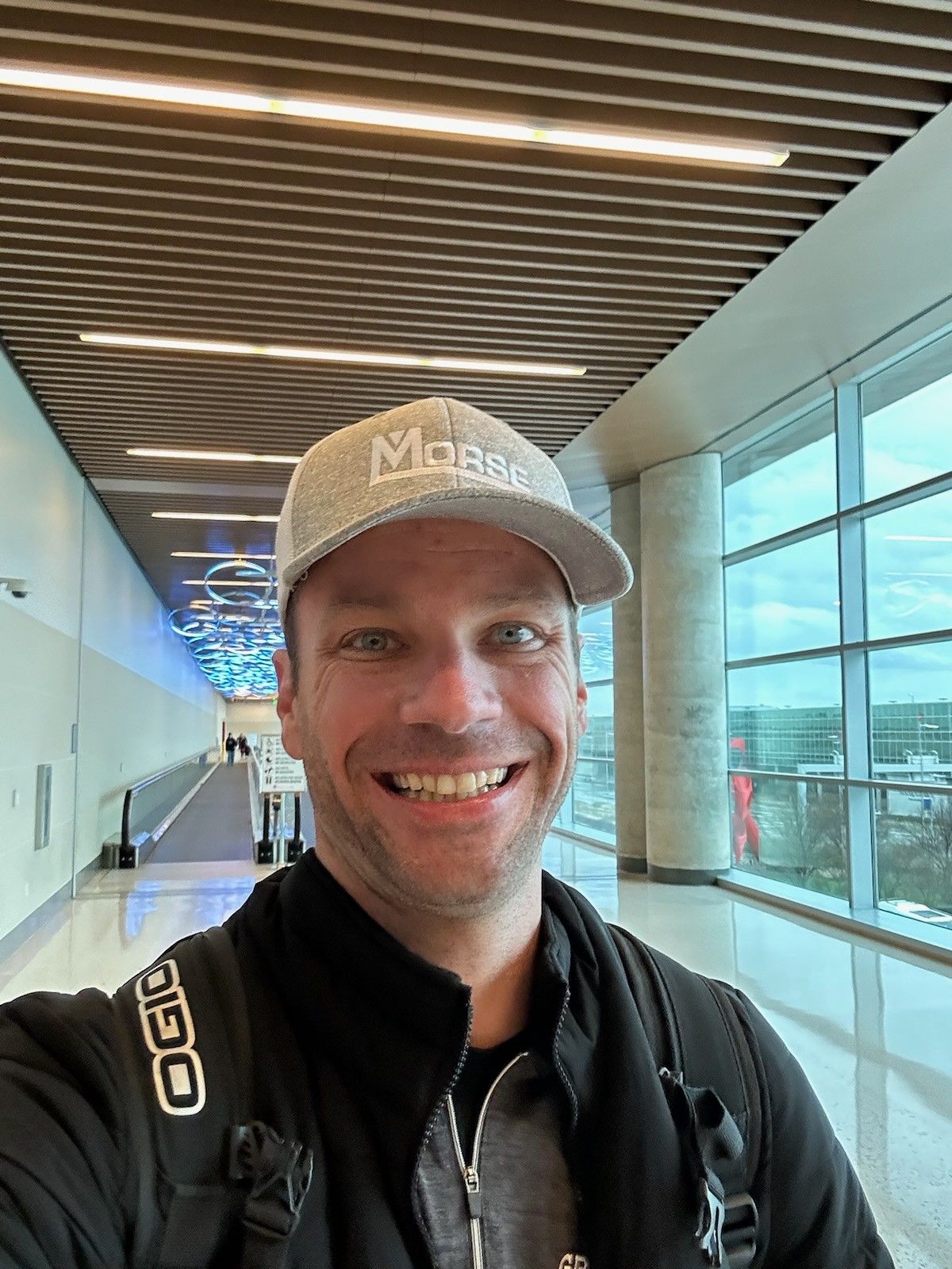 A man wearing a hat and a backpack is taking a selfie in an airport.