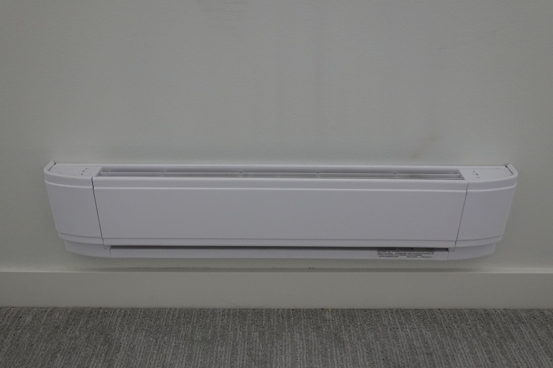 Radiateur plinthe blanc fixé sur un mur blanc dans une pièce.
