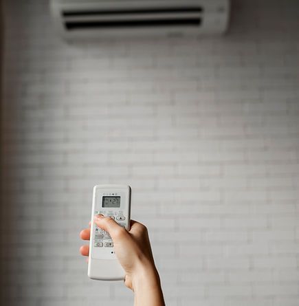 Main tenant la télécommande du climatiseur, pointée vers le climatiseur mural.