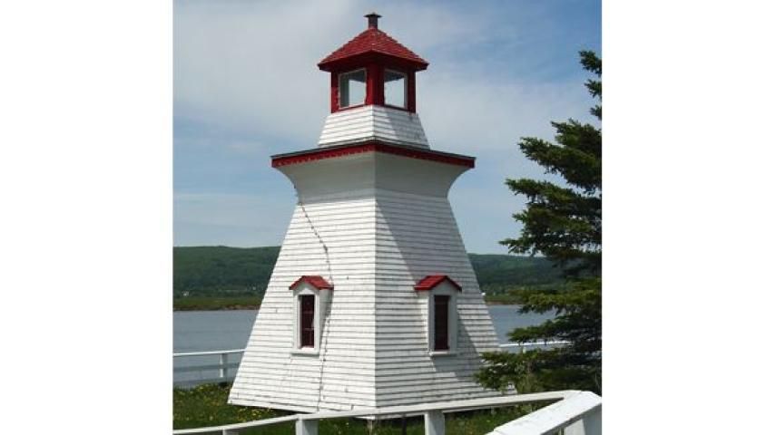 White lighthouse with red trim and cupola; outdoors near water, green vegetation.