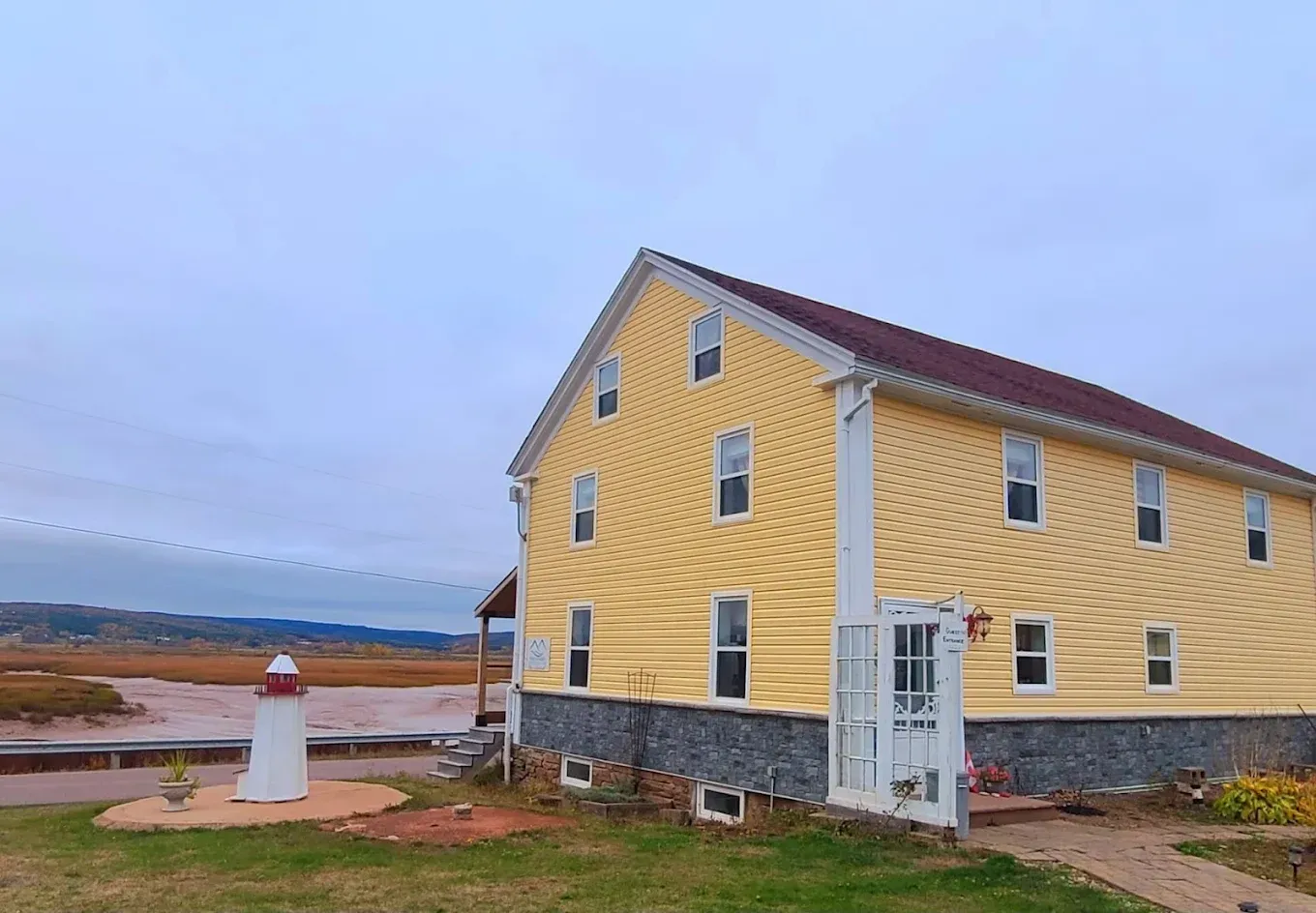 Yellow house and small lighthouse by a bay under overcast sky.