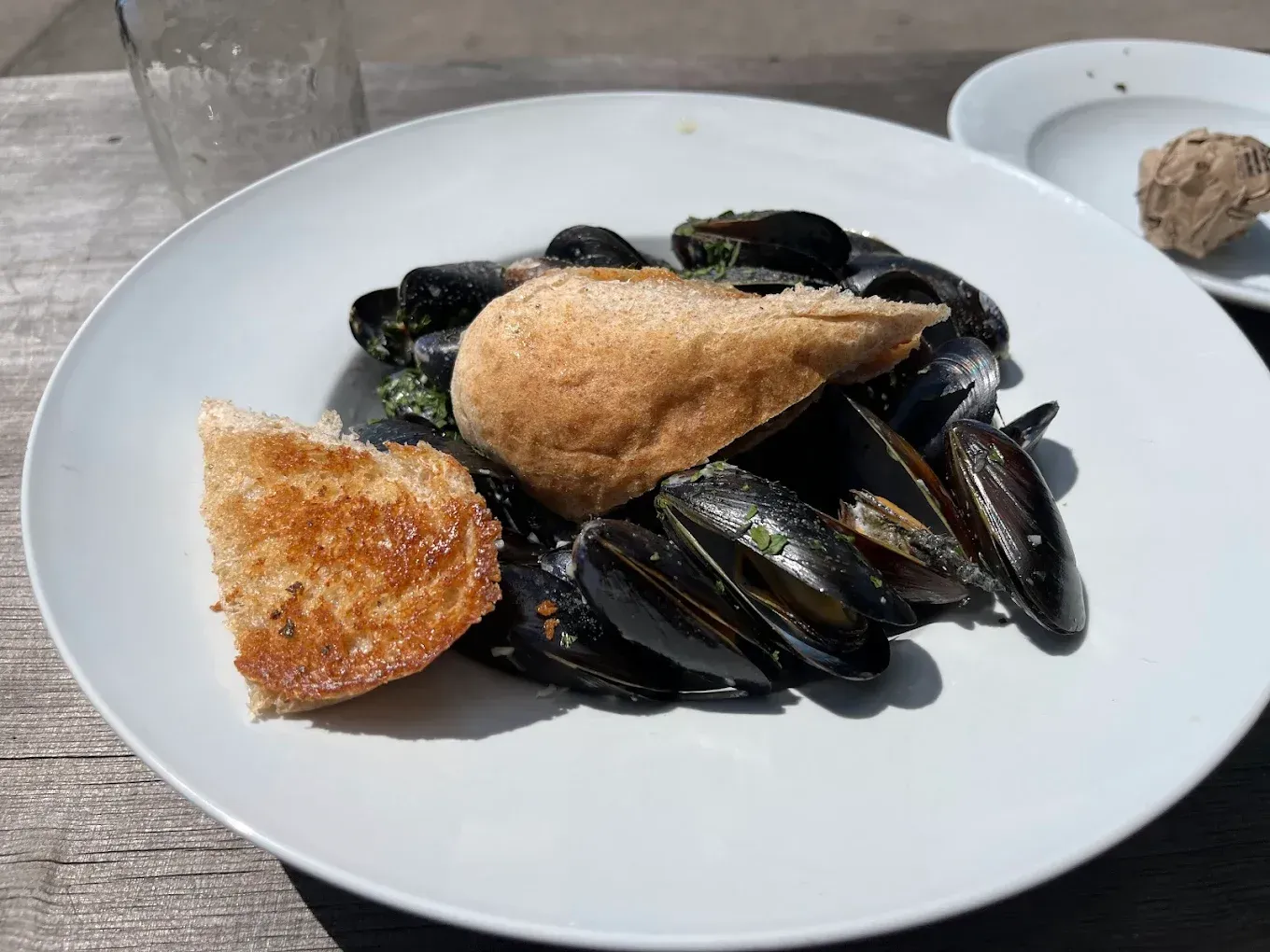 Mussels in a white bowl with toasted bread on a wooden table.