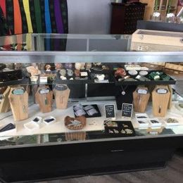 A glass display case in a store, filled with jewelry and stones. A rainbow flag hangs in the background.