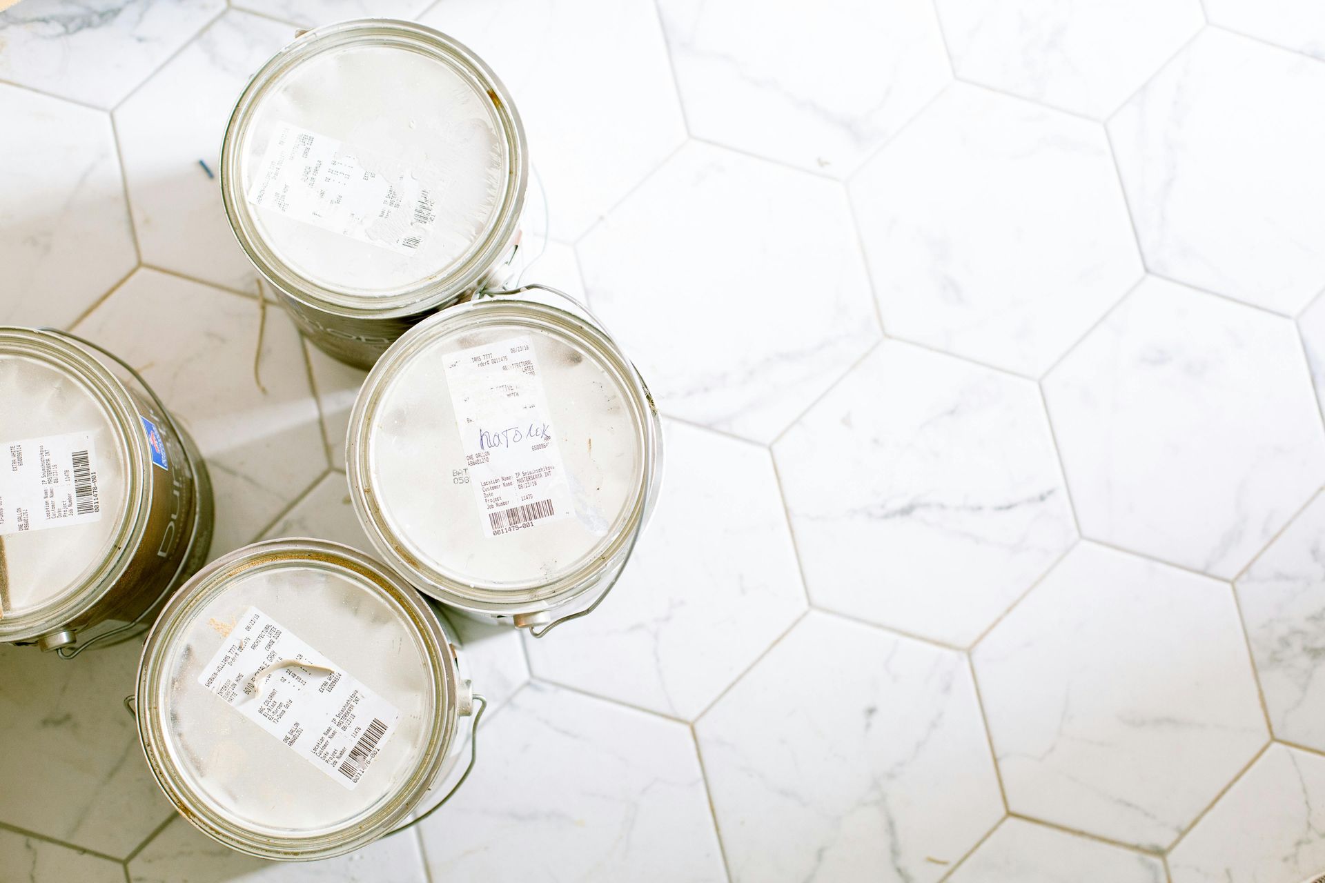 Overhead view of sealed paint cans on a white hexagonal tile floor.