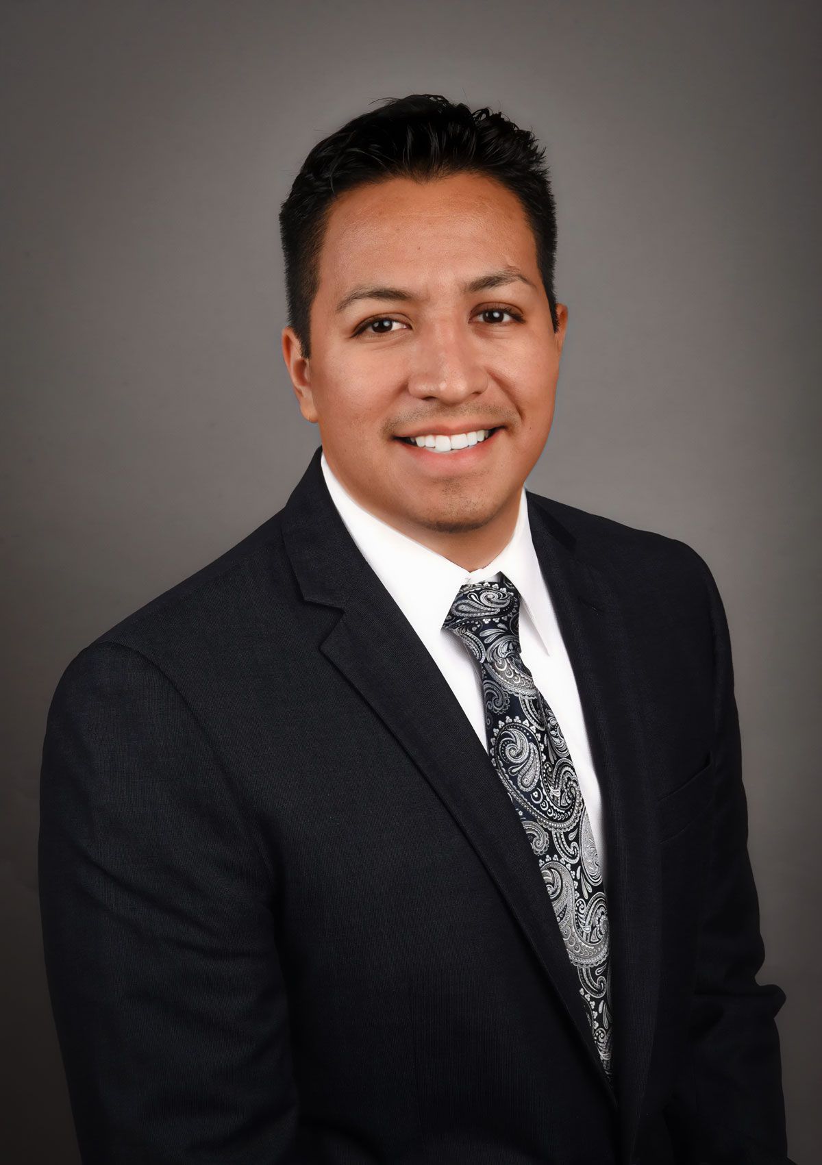 Dr. Gustavo Luna in a suit, smiling, headshot against a gray background.