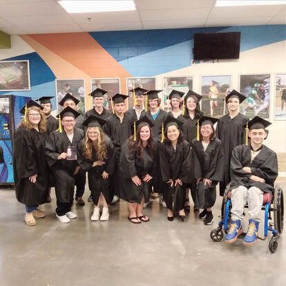 A group of students standing together in black graduation caps and gowns posing for the photo